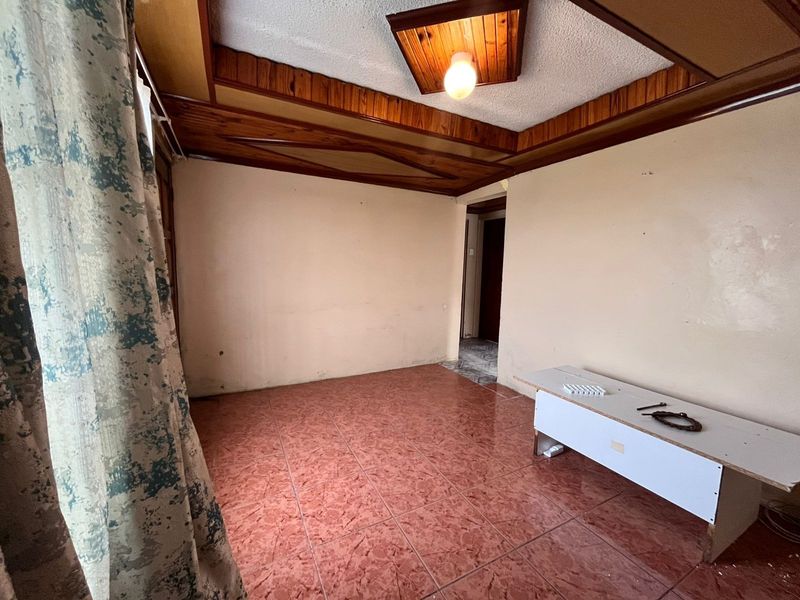 An empty living room featuring distinctive timber ceiling paneling and ceramic floor tiles, offering a blank canvas for renovation and interior design updates.