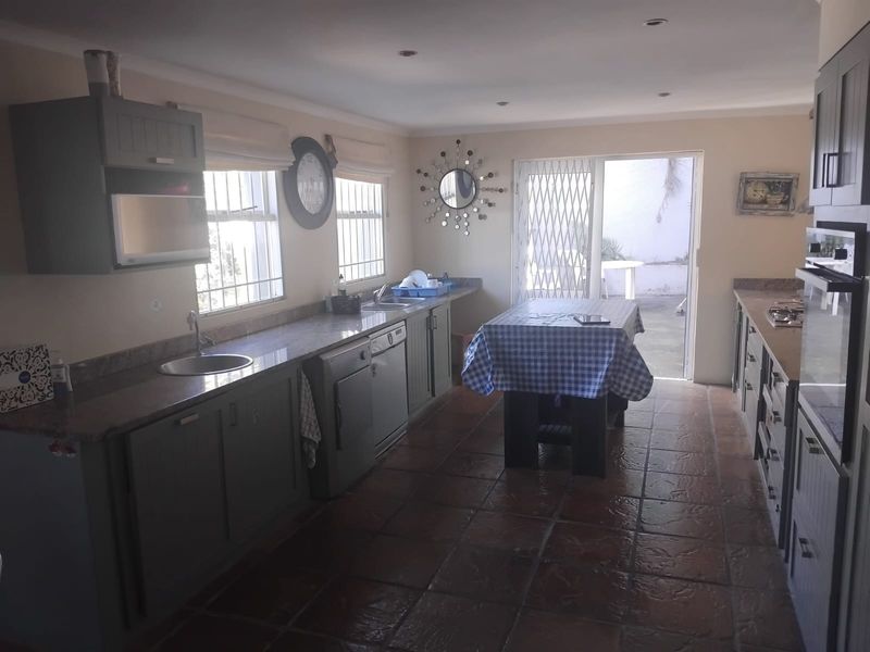 A functional kitchen featuring granite countertops, built-in oven, hob, and tiled flooring, with direct access to an outdoor patio area.