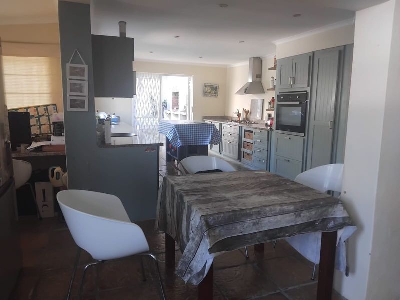 Open-plan kitchen and dining area featuring built-in cabinetry, integrated oven, extractor fan, stone countertops, and tiled flooring with access to the patio.