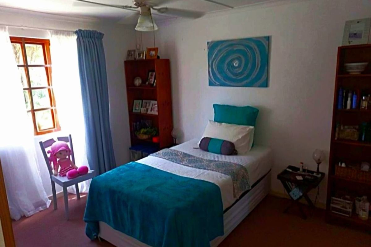 A standard bedroom featuring carpeted flooring, a ceiling fan, and a timber-framed window, providing a functional and lived-in space.