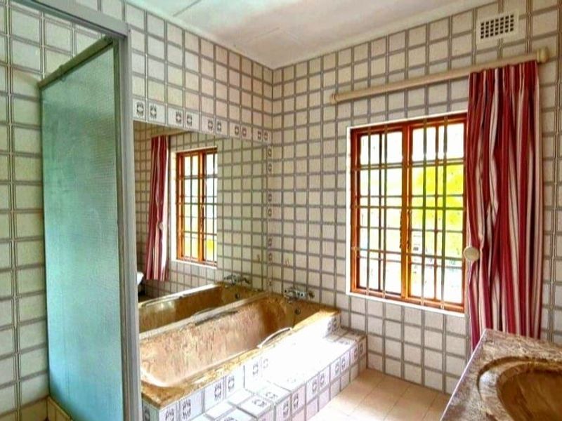 A dated bathroom featuring a built-in bathtub, vanity sink, and shower enclosure with full-height wall tiling and security-barred windows.