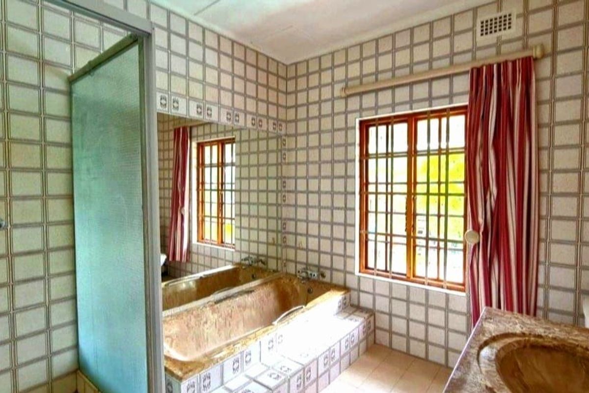 A dated bathroom featuring a built-in bathtub, vanity sink, and shower enclosure with full-height wall tiling and security-barred windows.