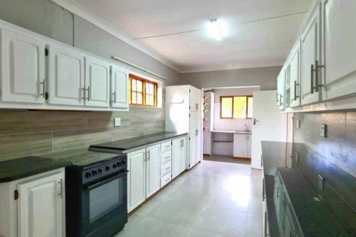 Spacious kitchen featuring white cabinetry, dark stone countertops, tiled backsplash, and a separate scullery area with additional sink and storage.