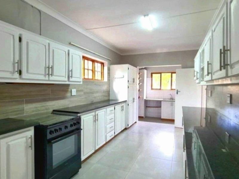 Spacious kitchen featuring white cabinetry, dark stone countertops, tiled backsplash, and a separate scullery area with additional sink and storage.
