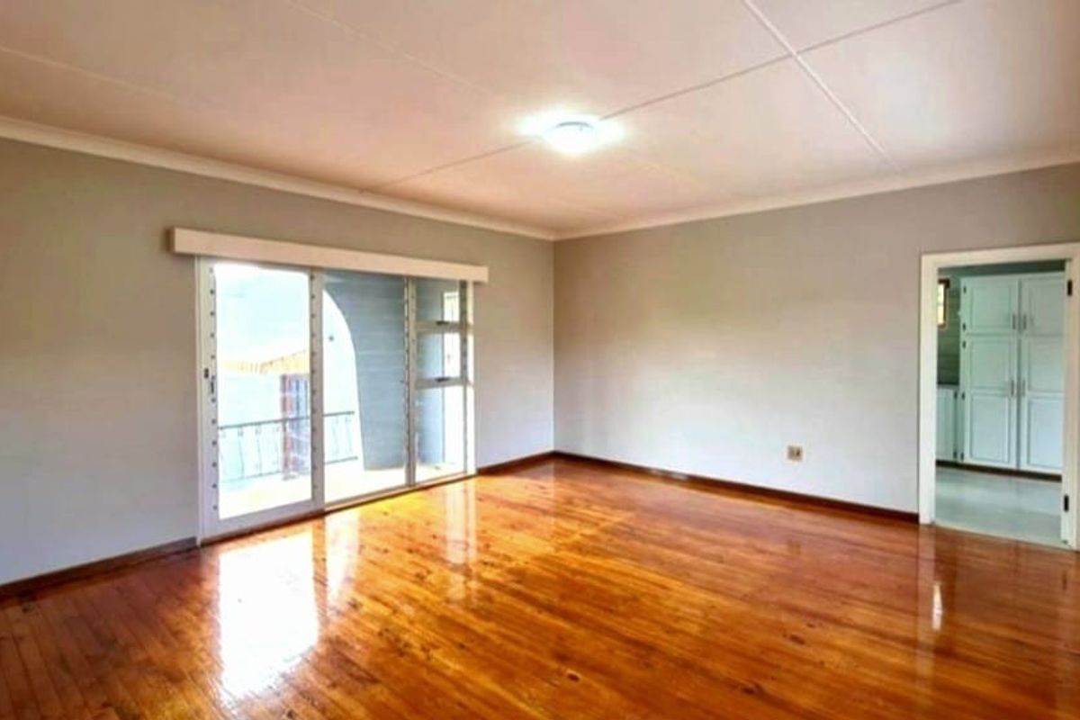 A bright, empty living room featuring polished hardwood flooring, neutral walls, and a sliding glass door leading to an outdoor area.
