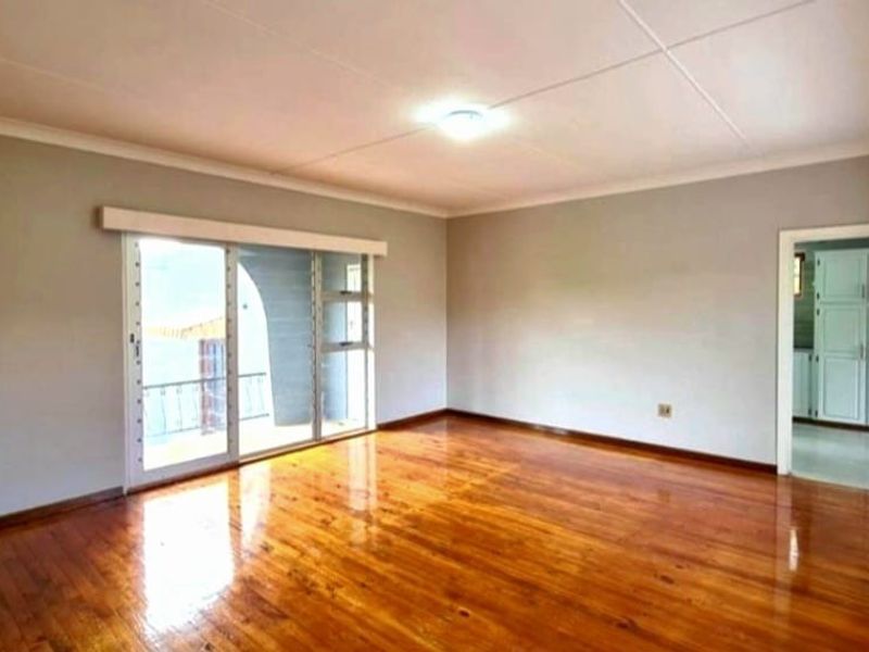A bright, empty living room featuring polished hardwood flooring, neutral walls, and a sliding glass door leading to an outdoor area.