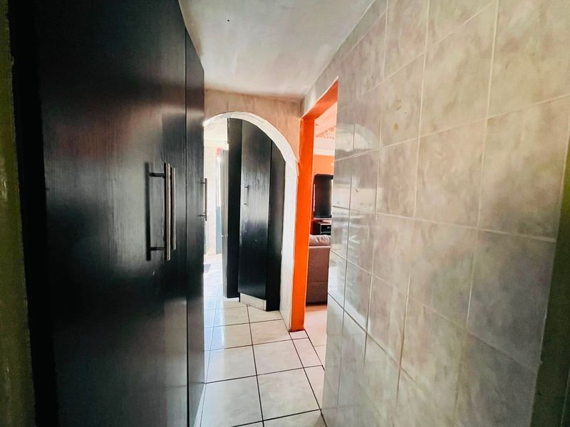 A narrow hallway featuring tiled flooring, built-in dark cabinetry, and an arched transition leading into the adjacent living area.