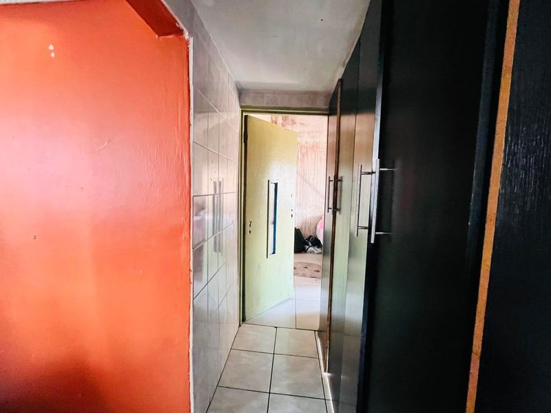 A narrow hallway featuring tiled flooring, wall tiling, and built-in storage cupboards, showing signs of wear and dated finishes.