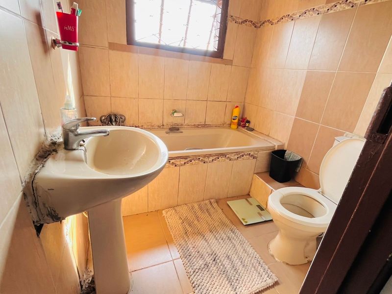 A compact bathroom featuring a pedestal basin, built-in bathtub, and toilet, finished with neutral ceramic tiling throughout.