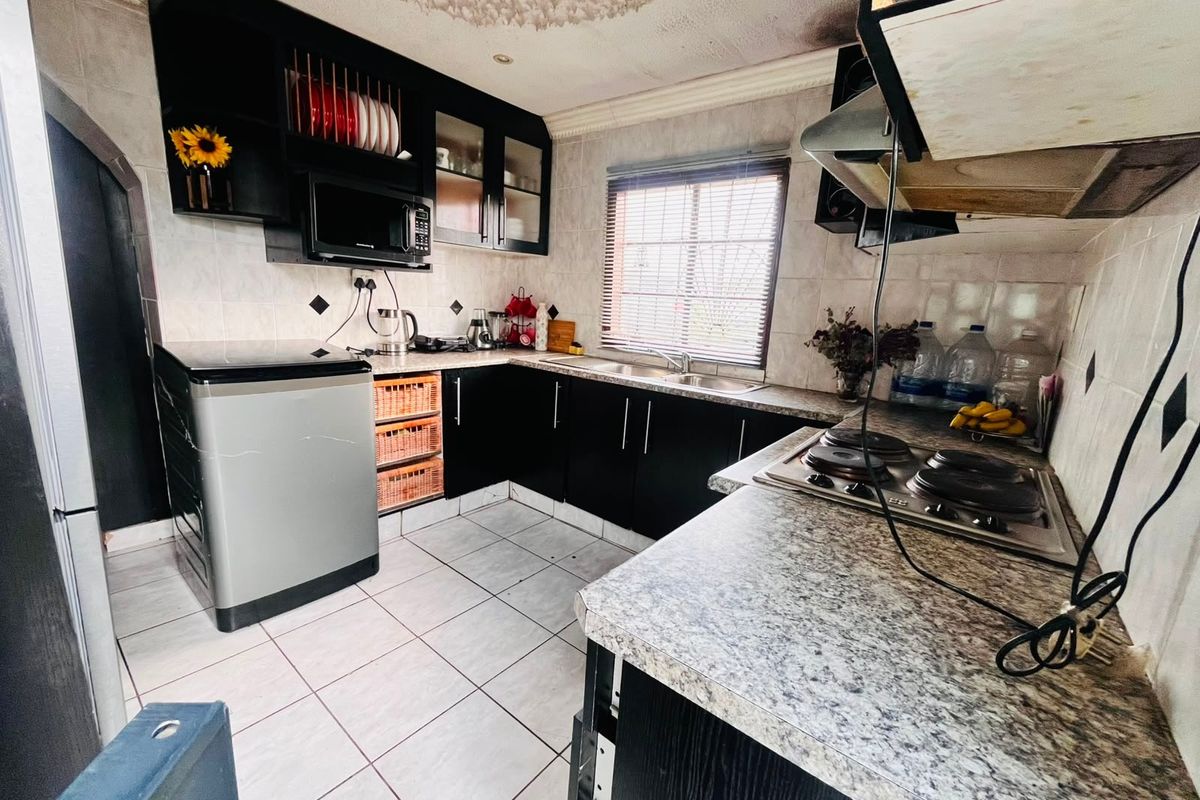 A compact kitchen featuring dark cabinetry, laminate countertops, a built-in hob, and tiled flooring, requiring some cosmetic updates to the ceiling and finishes.
