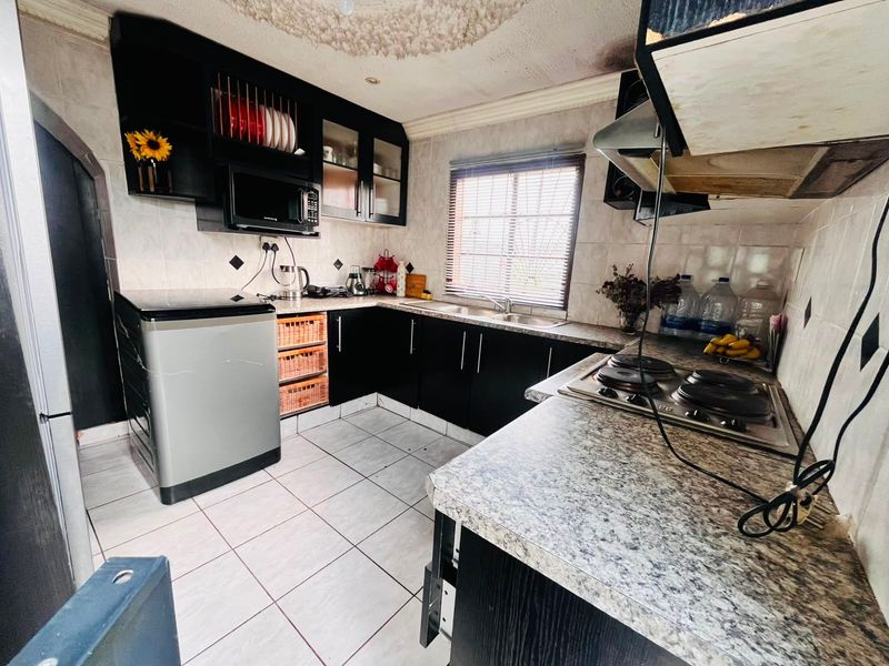 A compact kitchen featuring dark cabinetry, laminate countertops, a built-in hob, and tiled flooring, requiring some cosmetic updates to the ceiling and finishes.
