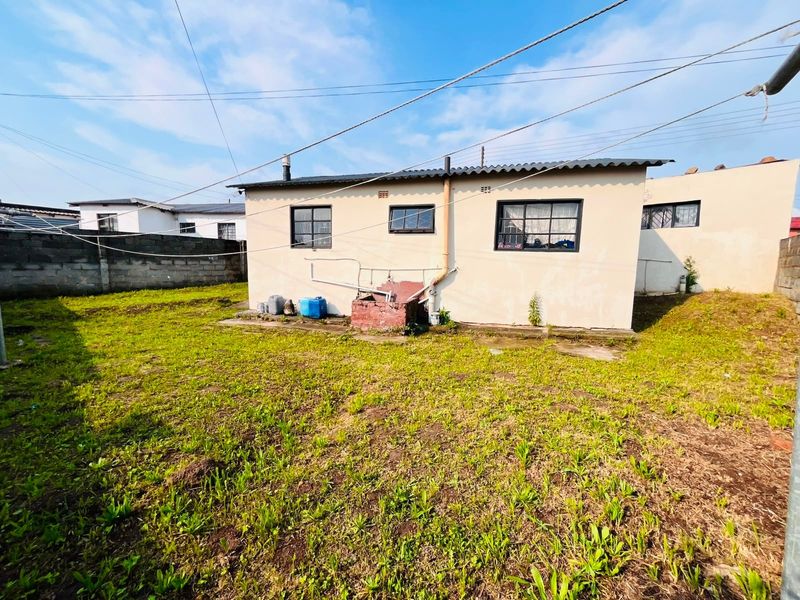 Rear view of the property showing the exterior facade, steel-framed windows, corrugated roof, and a large backyard area with perimeter boundary walls.
