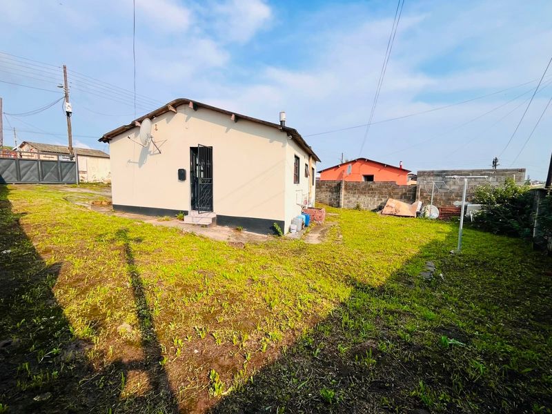 Rear view of the property featuring a modest garden, concrete block boundary walls, and a security gate entrance.