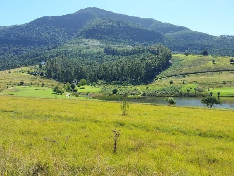 A scenic view of a vacant residential plot overlooking a lake, golf course, and mountain range.