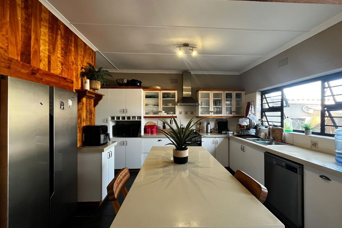 A well-maintained kitchen featuring a central island, ample built-in cabinetry, stainless steel extractor fan, and a wooden feature wall.