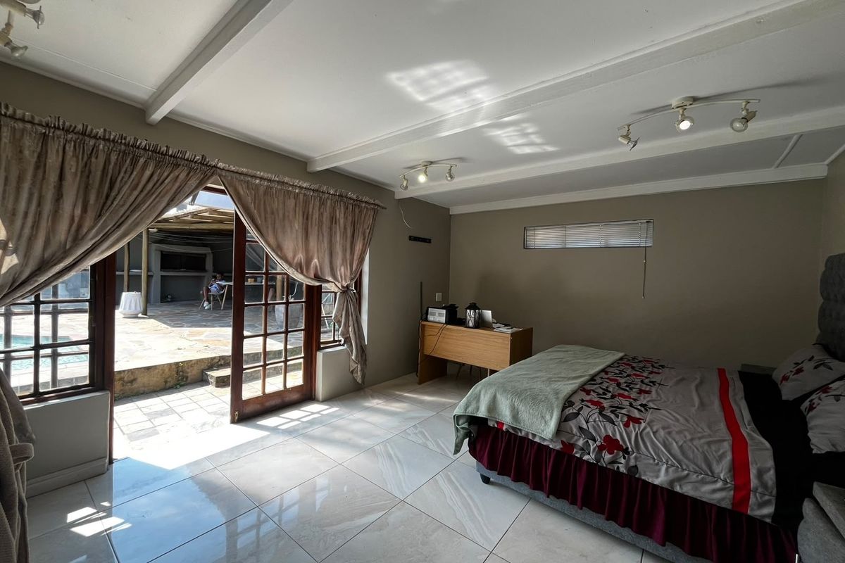 Spacious bedroom featuring large tiled floors, exposed beam ceiling, and direct access to an outdoor patio area through glass-paned french doors.
