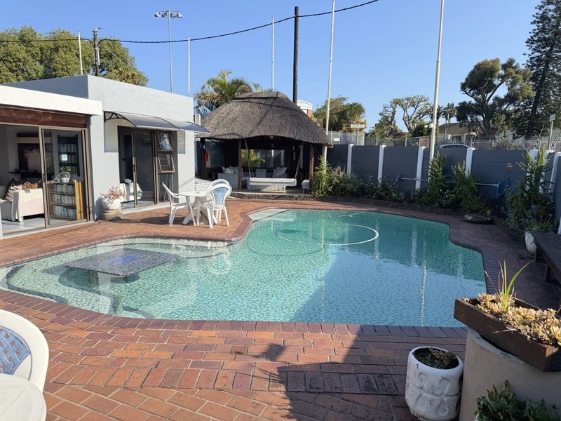Outdoor pool area featuring a swimming pool, brick paved surround, and a thatched gazebo, providing a functional space for outdoor relaxation and entertainment.