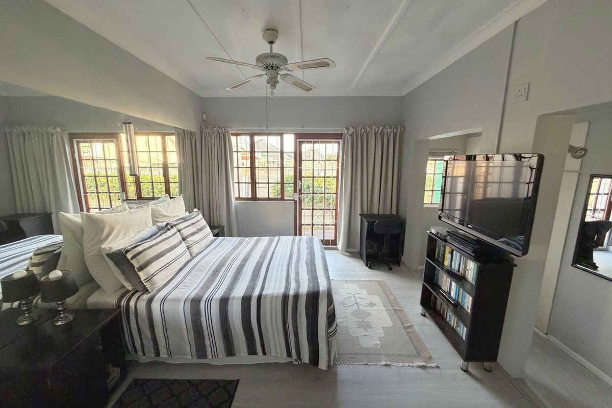 Spacious bedroom featuring a ceiling fan, large mirrored wall, and direct access to the exterior through a timber-framed door with security gate.