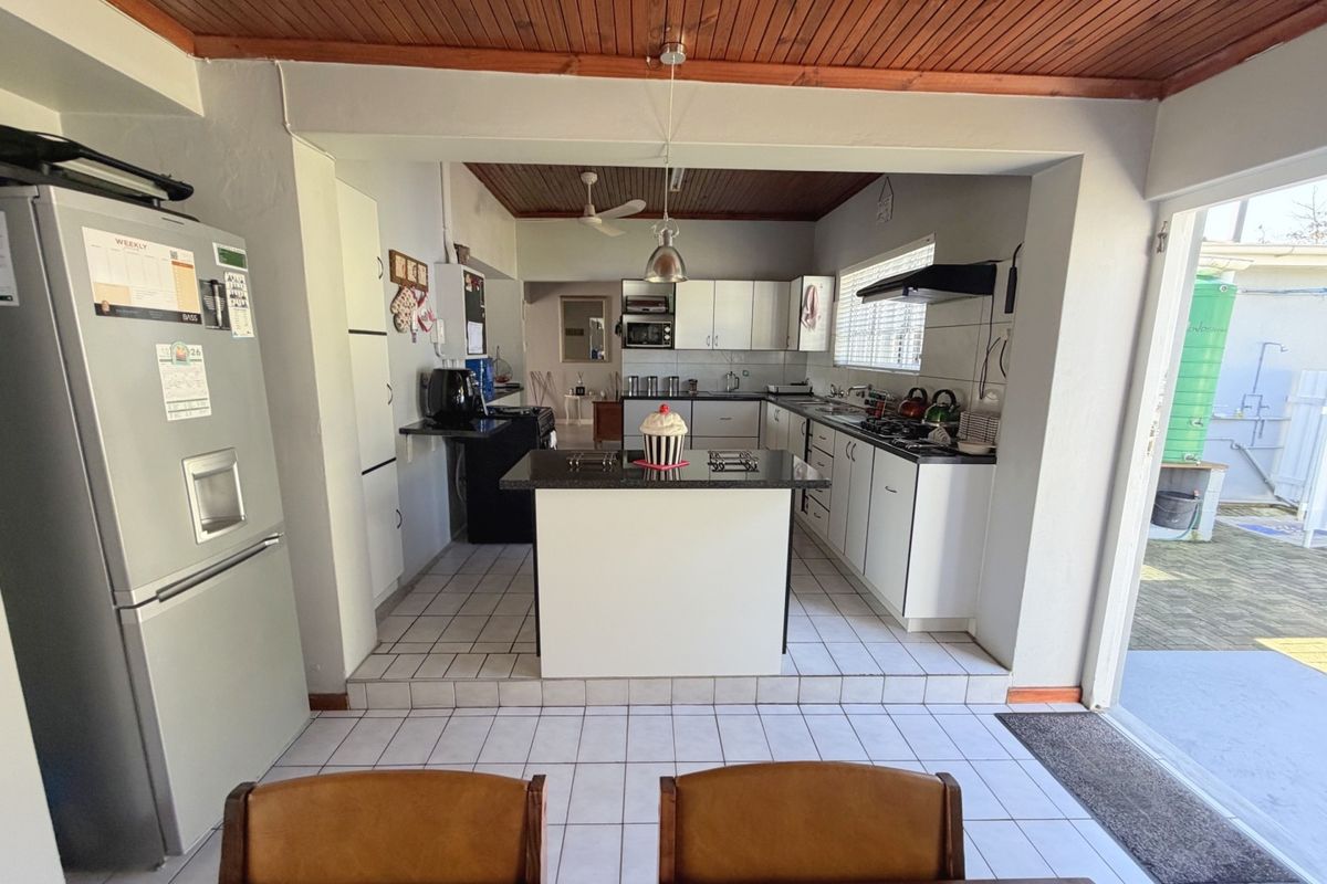 A functional kitchen featuring a central island, white cabinetry, tiled flooring, and a timber-paneled ceiling with direct access to the outdoor area.