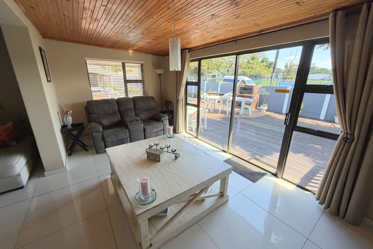 Bright living room featuring polished tile flooring, a warm timber-paneled ceiling, and large sliding glass doors providing seamless access to the outdoor patio area.