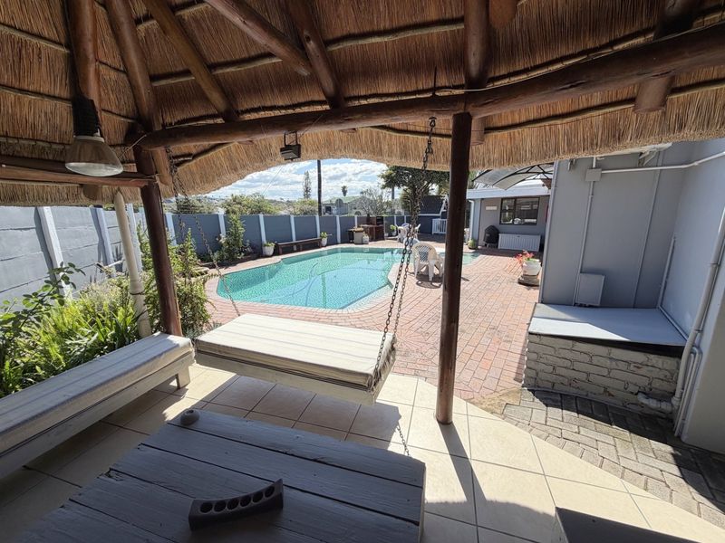Outdoor entertainment area featuring a covered thatched patio overlooking a swimming pool with brick paved surrounds and perimeter walling.