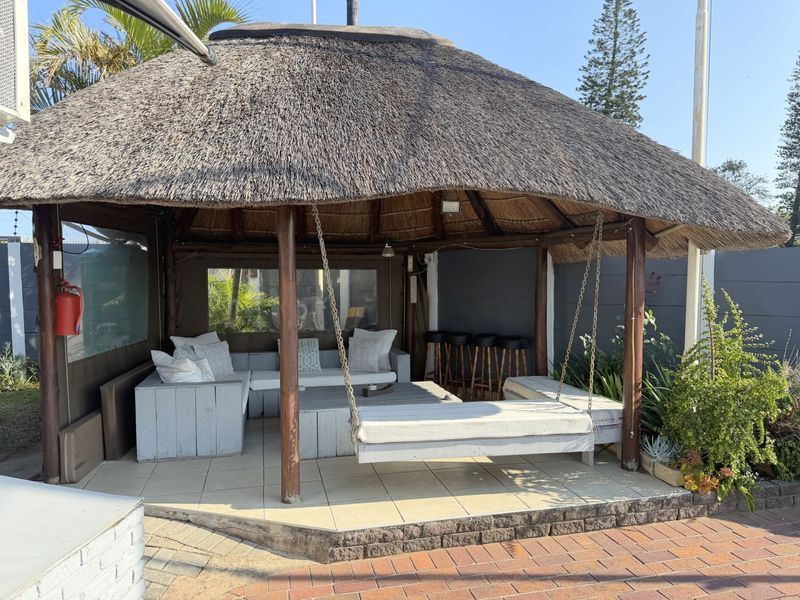 A covered outdoor entertainment area featuring a traditional thatched roof, timber support posts, and tiled flooring, ideal for relaxed outdoor living.