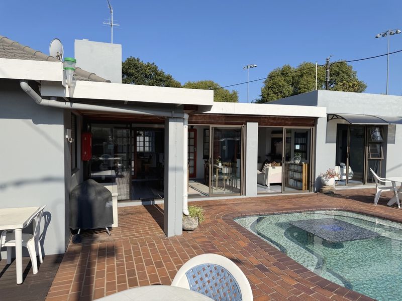 Rear exterior view featuring a brick-paved patio area, a swimming pool, and multiple sliding glass doors providing access to the interior living spaces.