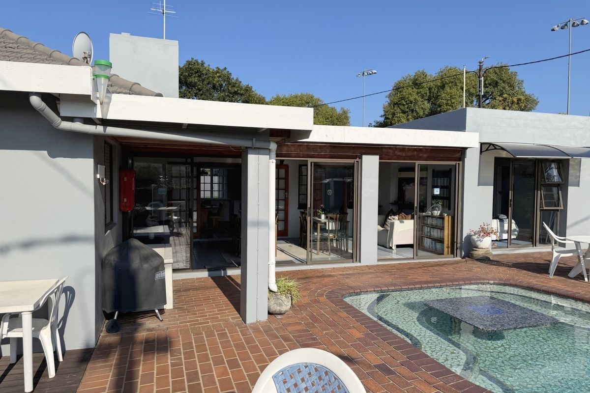 Rear exterior view featuring a brick-paved patio area, a swimming pool, and multiple sliding glass doors providing access to the interior living spaces.