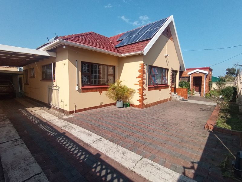 Front exterior view of a residential house featuring a paved driveway, carport, and roof-mounted solar panels.
