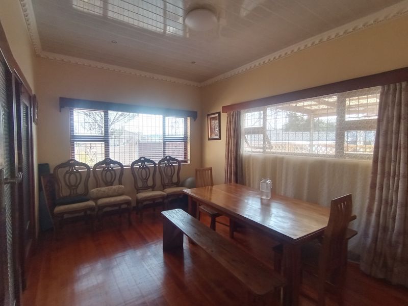 A dining room featuring hardwood flooring, decorative ceiling molding, and large windows fitted with security bars.