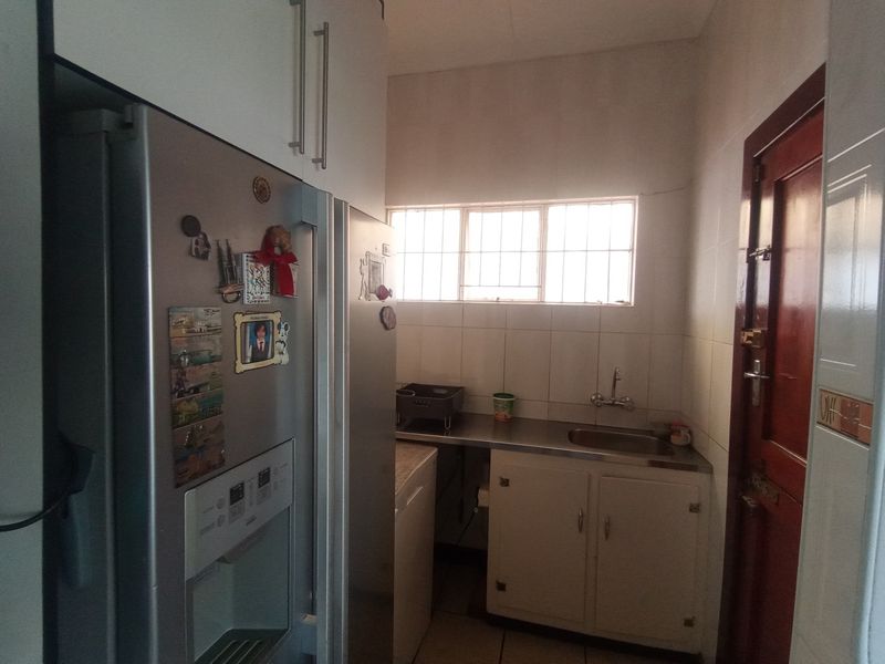 A functional scullery area featuring built-in cabinetry, a stainless steel sink, and tiled wall finishes, providing additional prep and wash-up space.