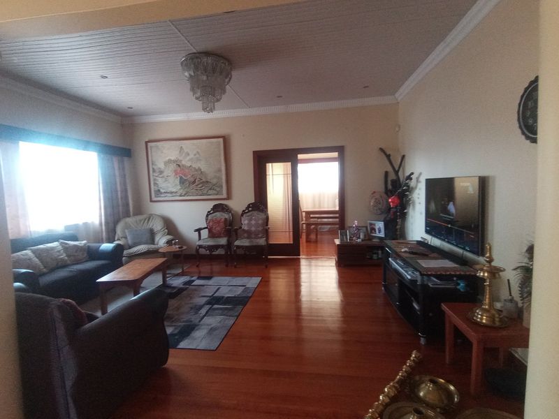 Spacious living room featuring polished hardwood flooring, crown molding, and a classic chandelier, with an open transition to an adjacent dining area.