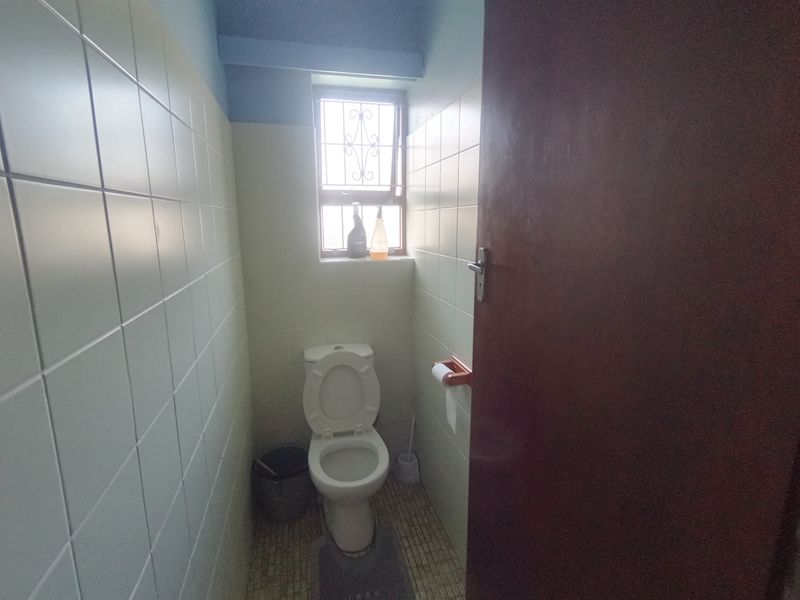 A compact bathroom featuring tiled walls and flooring, equipped with a standard toilet and a window with security bars.