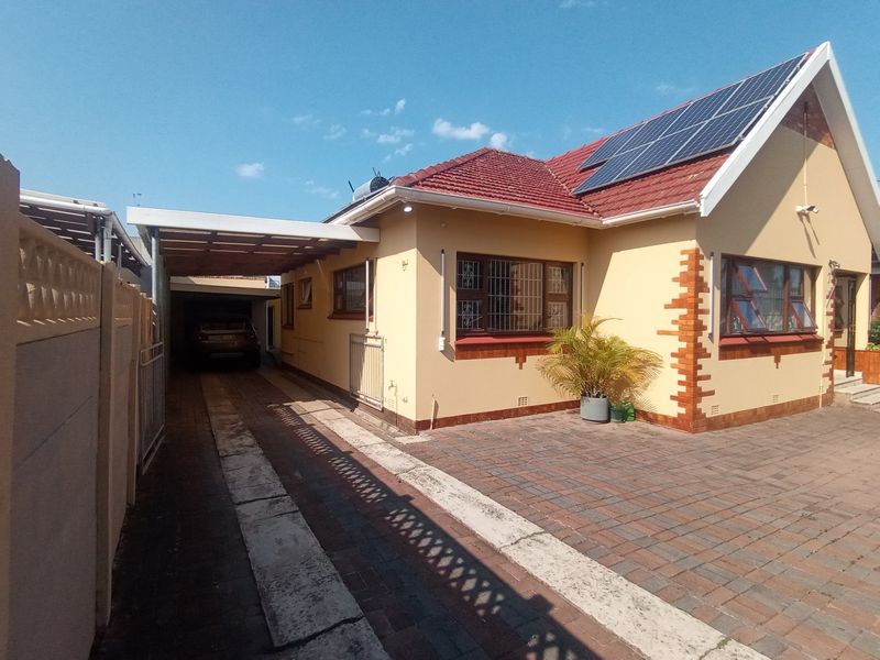 Front exterior view of a house featuring a paved driveway, carport, and roof-mounted solar panels with security bars on the windows.