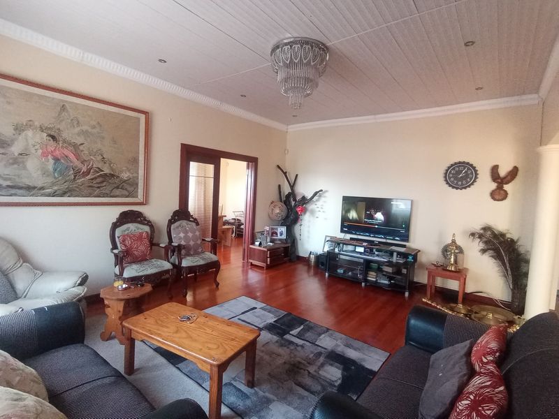 A spacious living room featuring warm timber flooring, a classic tongue and groove ceiling, and a decorative chandelier, offering a comfortable and traditional living space.