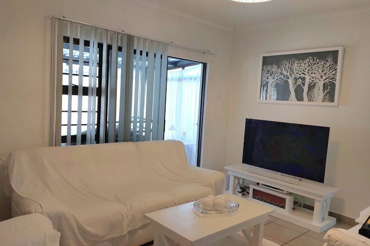 A bright living room featuring tiled flooring, vertical blinds, and a sliding glass door providing access to an outdoor area.