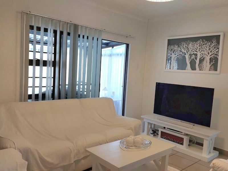 A bright living room featuring tiled flooring, vertical blinds, and a sliding glass door providing access to an outdoor area.