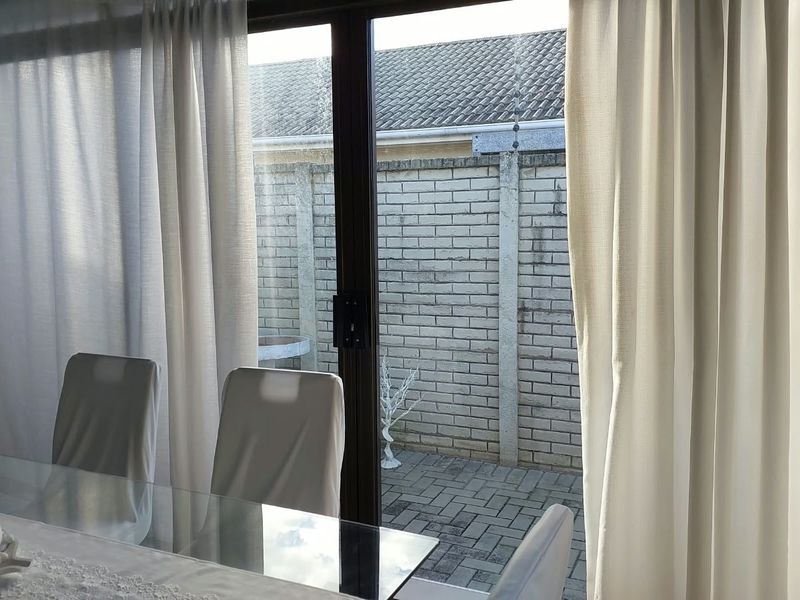 View from the living area through a sliding glass door leading to a private paved patio and enclosed garden space.