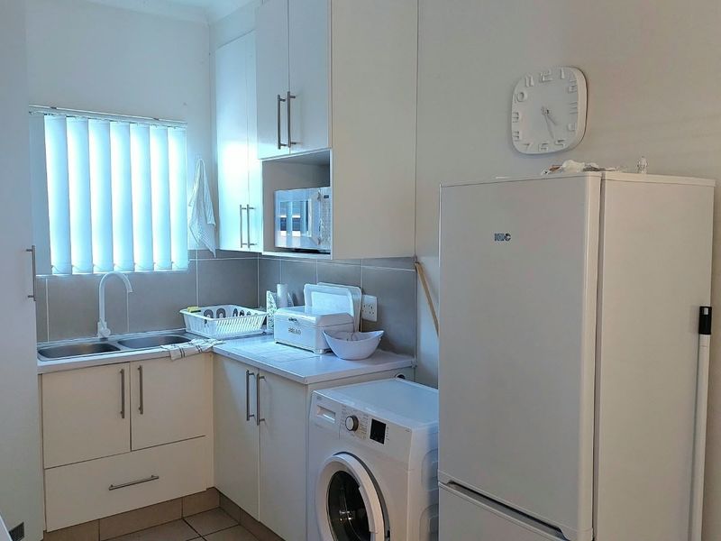 A functional kitchen featuring white built-in cabinetry, a double sink with mixer tap, tiled splashback, and integrated microwave space.