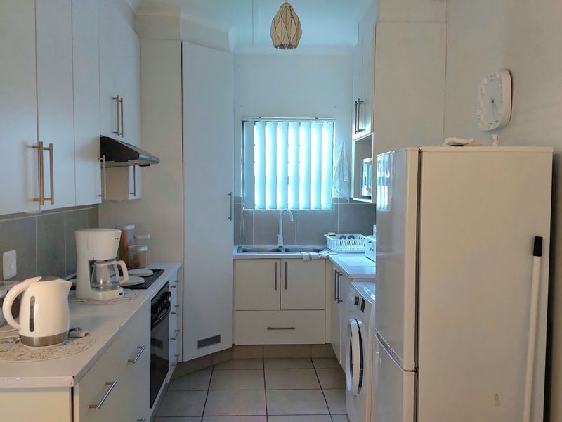 A functional kitchen featuring white built-in cabinetry, tiled flooring, a double sink, and integrated cooking appliances.