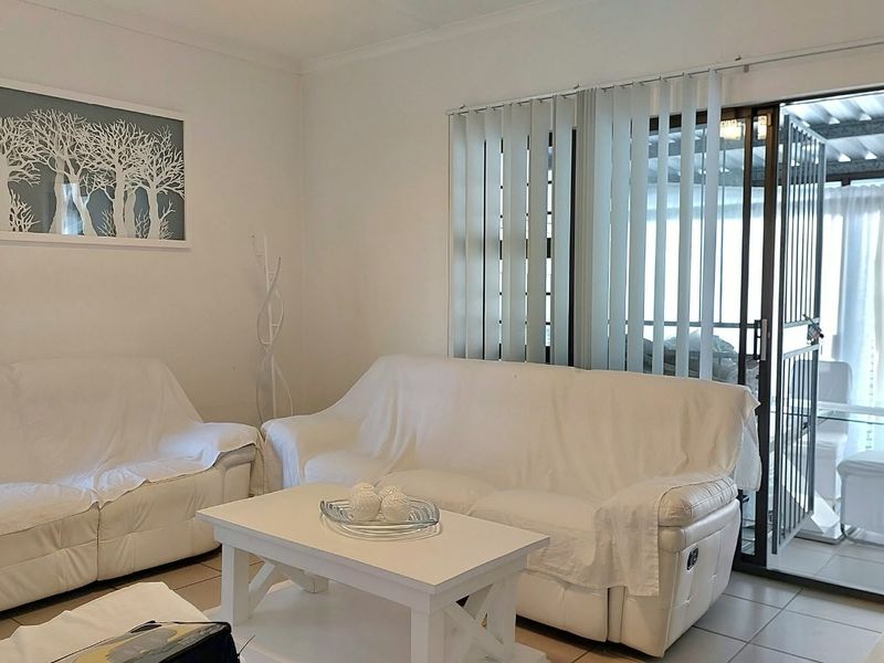 A bright living room featuring tiled flooring and a sliding glass door with vertical blinds, providing direct access to an outdoor patio area.