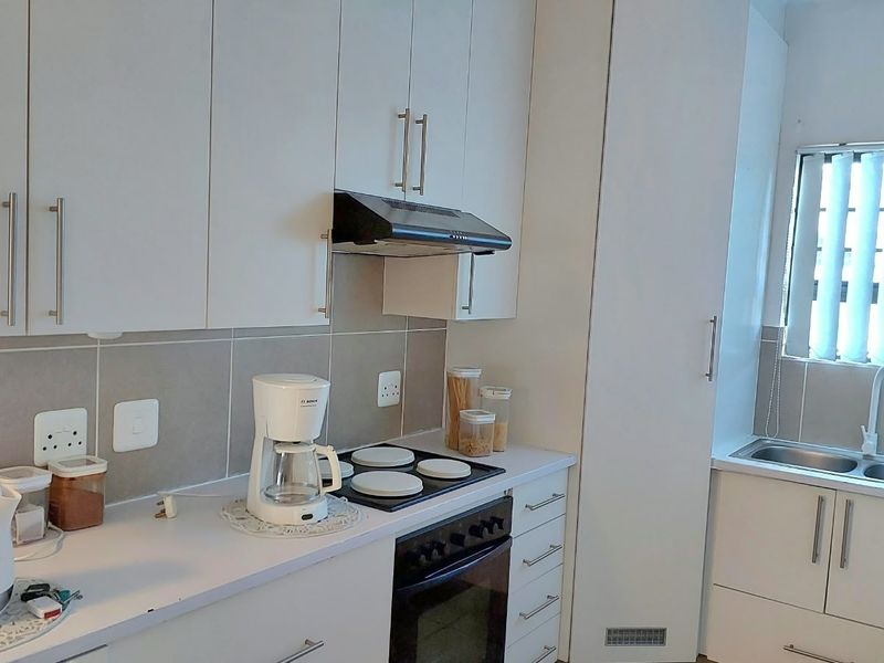A clean, modern kitchen featuring white cabinetry, a built-in oven with electric hob, extractor fan, and a stainless steel sink with tiled backsplash.