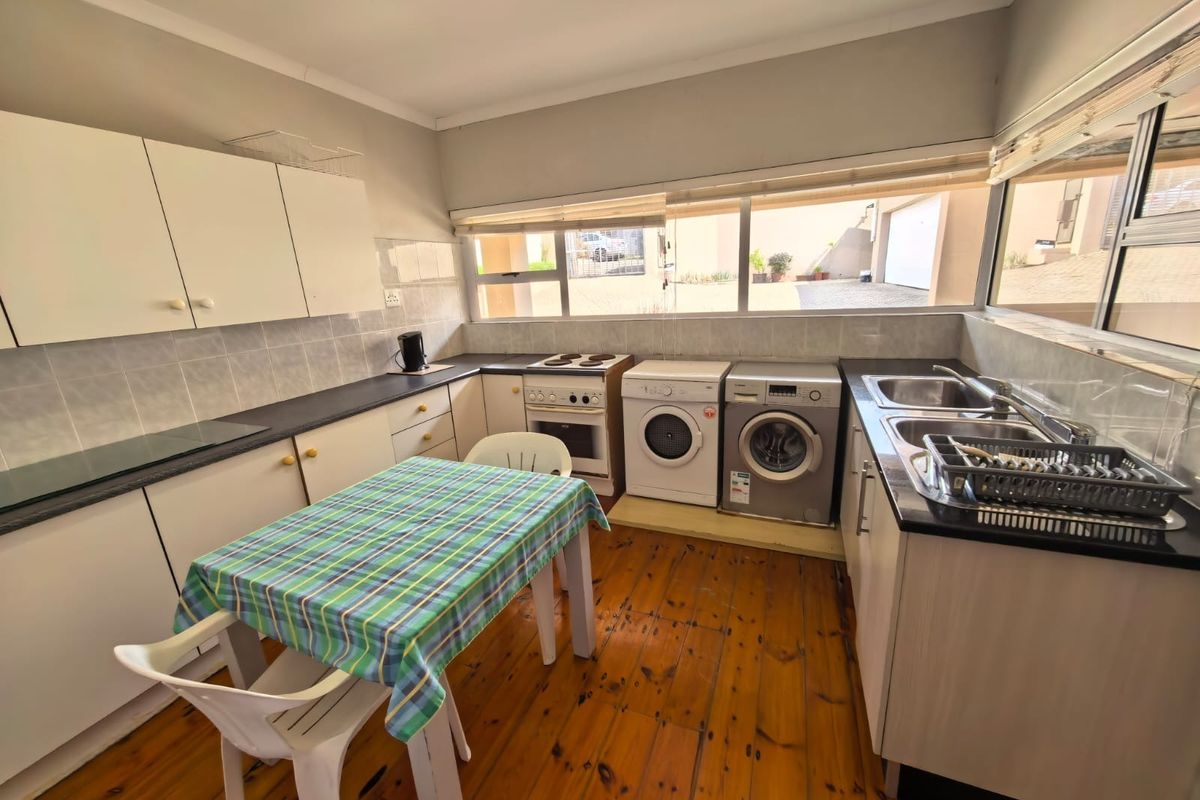 Functional kitchen featuring timber flooring, built-in cabinetry, laminate countertops, a double stainless steel sink, and a freestanding electric stove with integrated laundry appliance space.