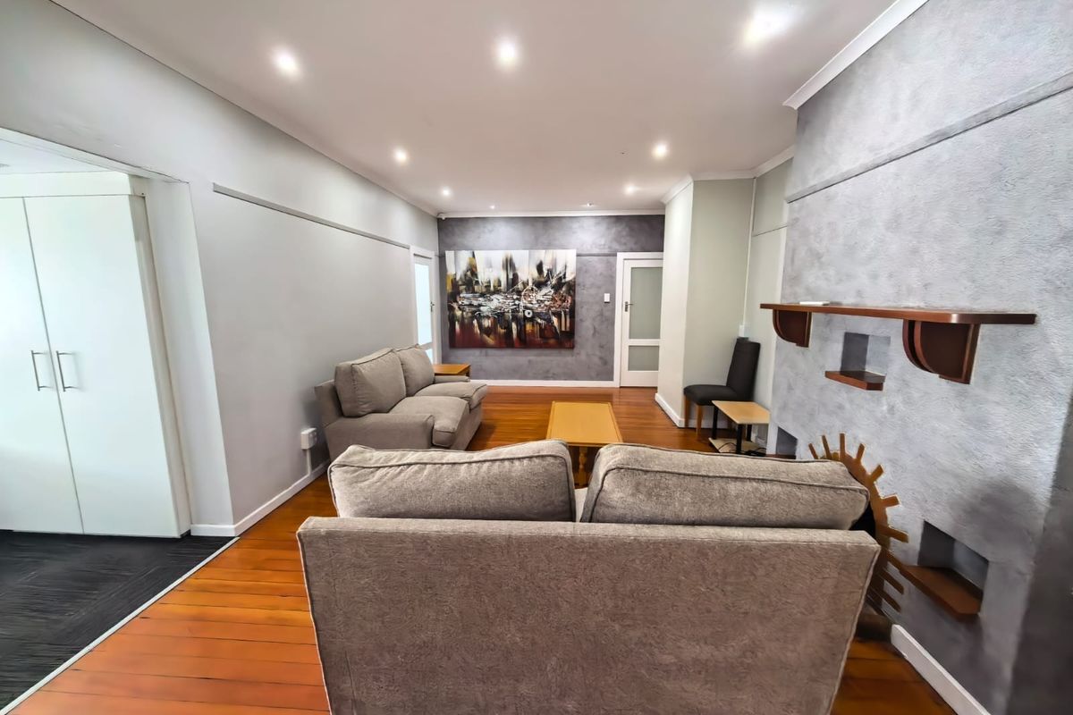 Spacious living room featuring polished hardwood flooring, recessed downlighting, and a prominent built-in fireplace with a decorative mantelpiece.