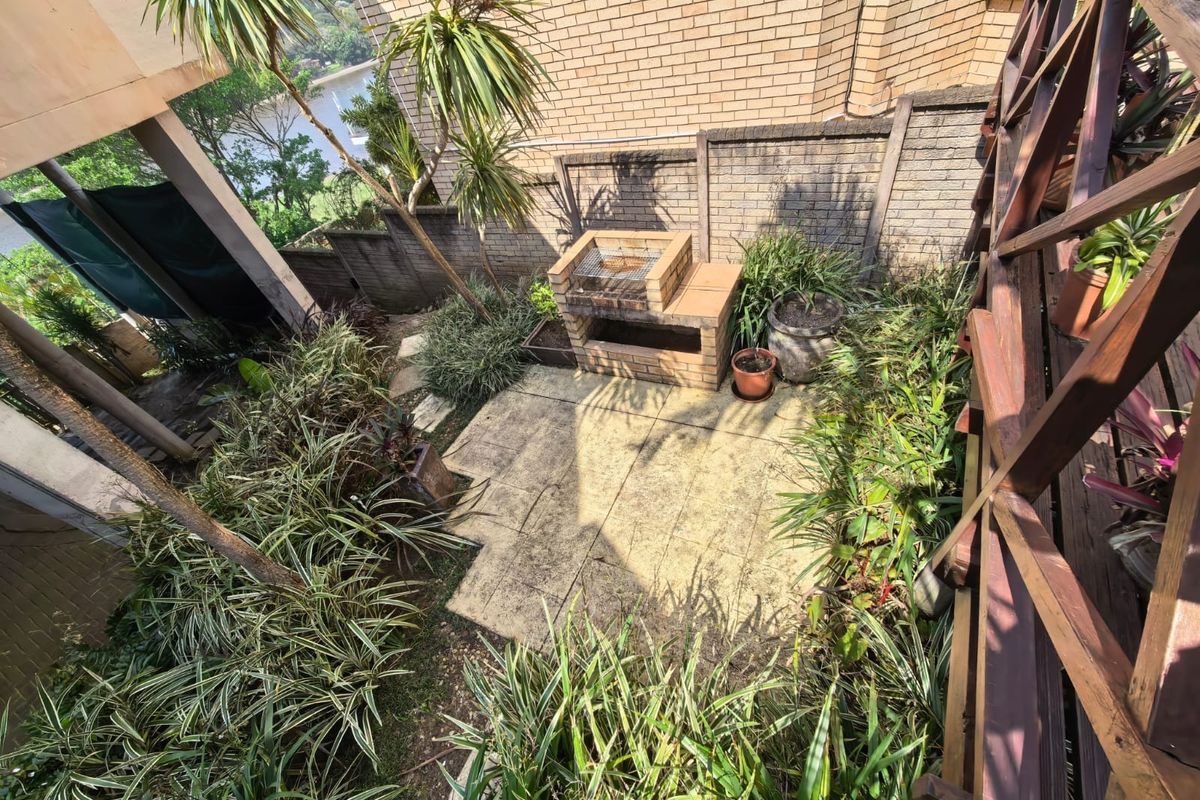 Rear garden area featuring a brick built-in braai, paved patio space, and established garden beds enclosed by brick boundary walls.