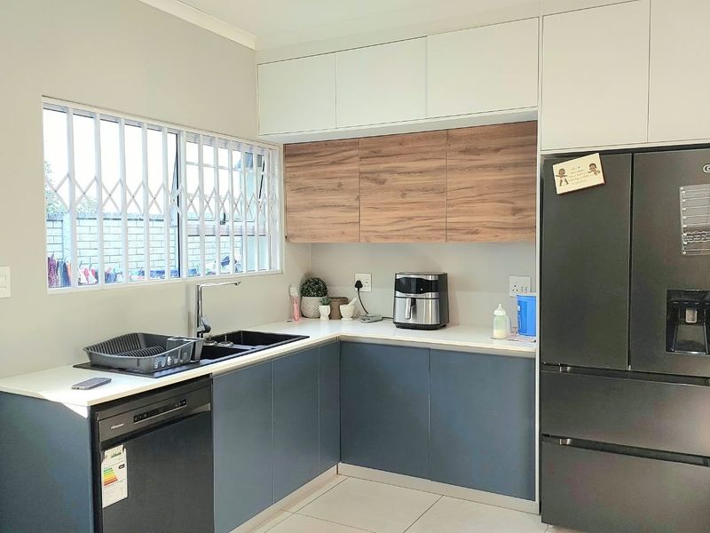 Modern kitchen featuring two-tone cabinetry, laminate countertops, integrated sink, and tiled flooring with a security gate on the window.
