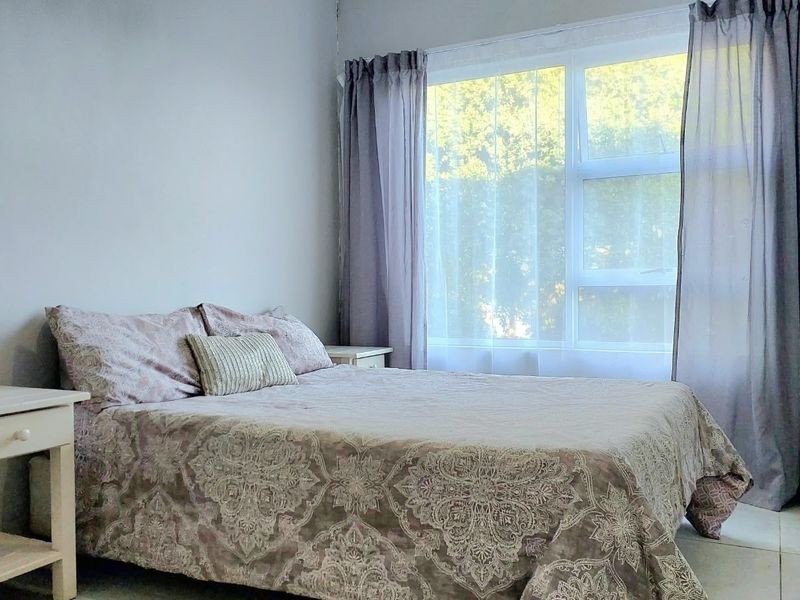 A bright bedroom featuring tiled flooring, a large window for natural light, and a built-in wardrobe for storage.
