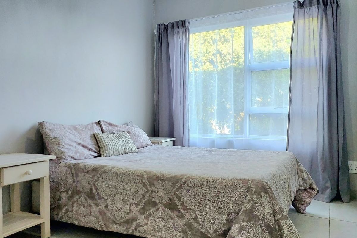 A bright bedroom featuring tiled flooring, a large window for natural light, and a built-in wardrobe for storage.