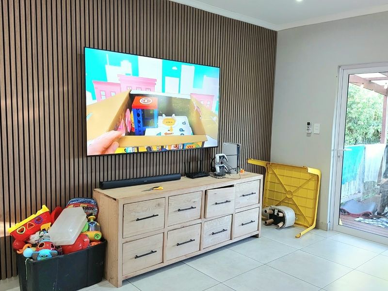 Living room featuring a modern slatted timber feature wall, tiled flooring, and direct access to an outdoor patio area through double glass sliding doors.