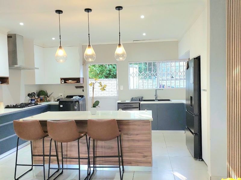 Modern kitchen featuring a central island, built-in oven, gas hob, sleek cabinetry, and stylish pendant lighting, finished with contemporary tiled flooring.